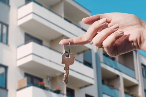 Real estate agent holding keys to new condo in front of building - purchasing a condominium concept